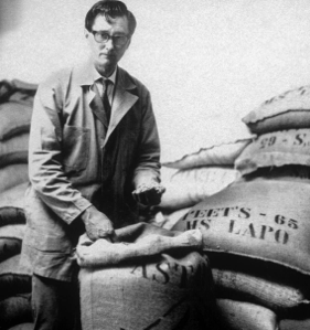 Alfred Peet posing with several stacked bags of coffee beans